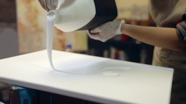 Women artists pouring white glue on the canvas. Artistic collaboration in workshop.