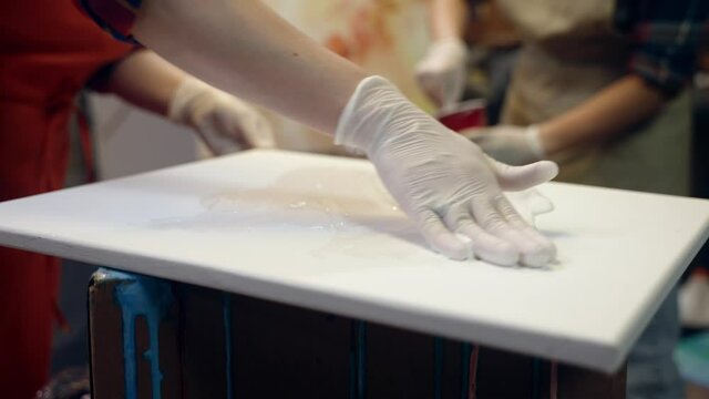 Women artists smering white glue on the canvas. Artistic collaboration in workshop.