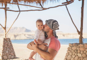 Father kisses his newborn daughter under a straw awning in the desert