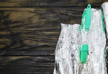 Roll of aluminum foil with a silicone brush on a wooden table. For cooking food.