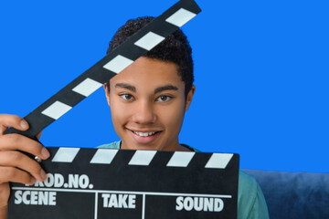 African-American teenager with clapperboard near color wall