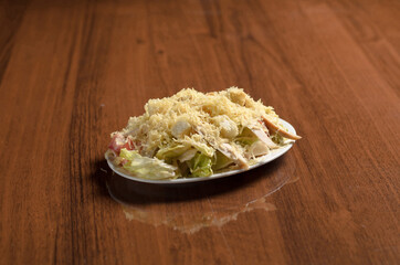 Salad with chicken meat, breadcrumbs, tomatoes, salad leaves with mayonnaise and cheese in a white plate on the table