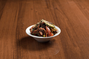 Korean salad with eggplant, cucumbers, tomatoes, carrots and sesame seeds in a white plate on the table