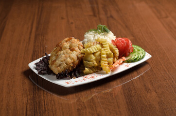 Chicken cutlet in Kiev breaded in breadcrumbs, with rice, French fries, tomatoes and cucumbers in a white plate on the table
