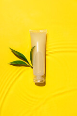 Tube of cosmetic product in water on color background