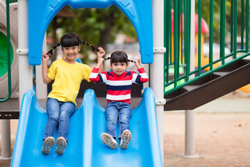 Cute little girls siblings having fun on playground outdoors on sunny summer day