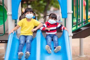 Fototapeta na wymiar new normal lifestyle, social distancing concept. happy kids wearing face mask having fun on at playground protect coronavirus covid-19,