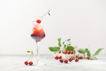 Cherry liqueur with ice and berries on a gray background. A refreshing summer alcoholic drink