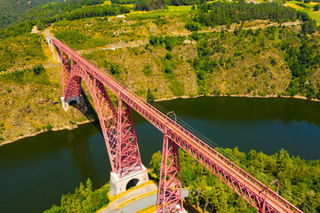 Scenic drone view of parabolic arched framework of railway bridge Viaduc de Garabit across river Truyere near Ruynes-en-Margeride in Auvergne, France.. - obrazy, fototapety, plakaty