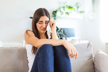 Unhappy young woman covering face with hands, crying alone close up, depressed girl sitting on couch at home, health problem or thinking about bad relationships, break up with boyfriend, divorce