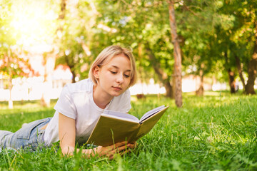 Girl teenager lies on the lawn and reads a book. 