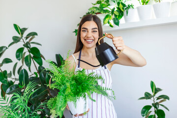 Joyful young woman enjoys her time at home and watering her plant by the window at home. woman takes care of her fern water on the tree on a relaxing day in the garden at home. © Graphicroyalty