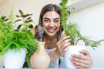 Woman caring for plants next to steam aroma oil diffuser on the table at home, steam from...