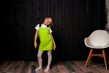 Cute little girl staying on a black wooden background. Space for text.