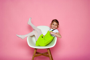 Attractive girl sitting on the white chair on the pink background.
