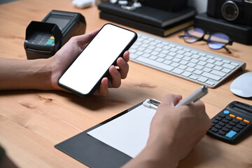 Businessman checking information on mobile phone and making note on notepad.