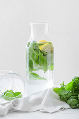 Bottle of lemonade with basil on light background