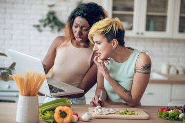 Emotional questioning girlfriends looking indignant at laptop