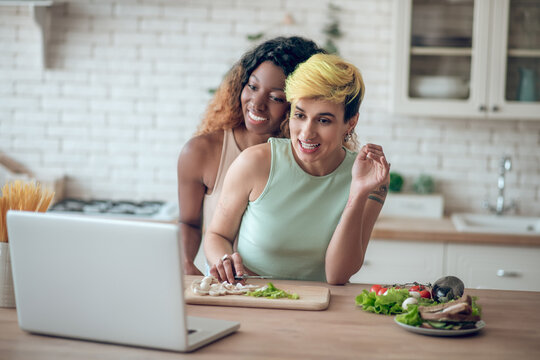 Couple of girlfriends preparing breakfast looking at laptop - Powered by Adobe