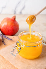 Honey pouring from dipper into glass jar and pomegranate on light background, closeup