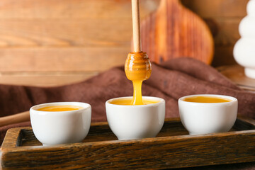 Honey pouring from dipper into bowls on wooden background, closeup