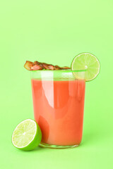 Glass of bloody mary cocktail garnished with bacon and lime on color background