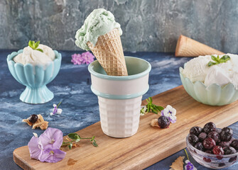 Still life with pistachio and creamy ice cream in vases and cone on blue background