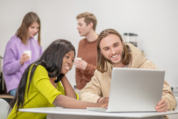 Darkskinned girl and caucasian guy interestedly looking at laptop