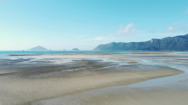 A tropical island in southeast Asia with a coastal area during a low tide. People are walking by the intertidal zone. The man is driving a motorbike on the sandy beach