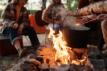 Fototapeta premium Close-up of food preparing in a pot on a fire with people sitting in the background