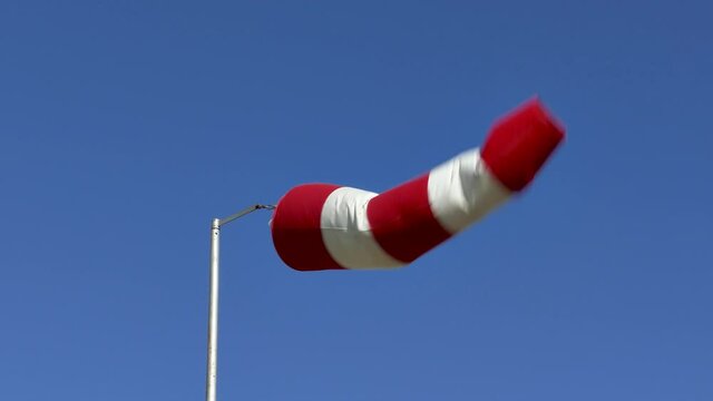Windsock flutters in a strong wind showing wind direction and speed against perfect blue sky on clear summer day.