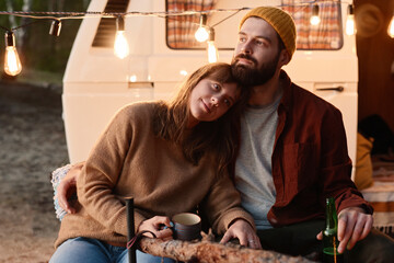 Romantic young couple sitting near the fire and drinking tea during picnic in the forest