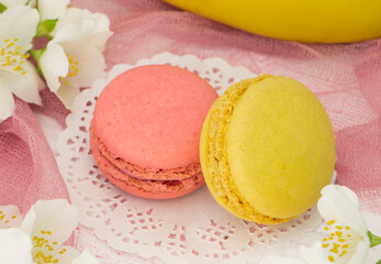 two French macaroons, pink and yellow on a pink background with flowers and a banana. Banana and raspberry macaroon are close. Fragrant macaroons concept. High quality photo