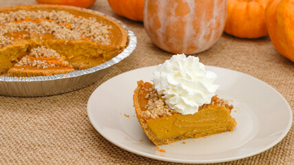 Slice of fresh baked homemade pumpkin pie decorated with crushed nuts and orange zest close up on a plate with whipped cream