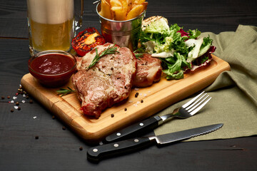 Grilled roated beef steaks, potato and sauce on wooden cutting board