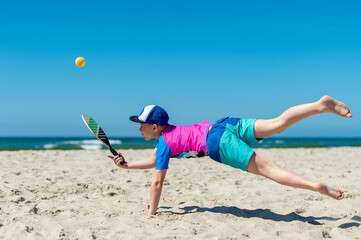 Young boy playing tennis on beach. Summer sport concept.