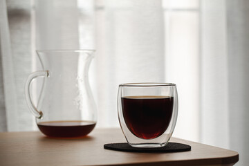 Glass of coffee paired with a coffee mug On the desk by the balcony in the dim light
