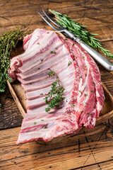 Lamb raw ribs rack in wooden tray with herbs. wooden background. Top view