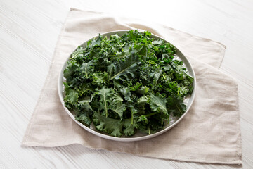 Raw Organic Baby Kale on a gray plate on a white wooden surface, side view.