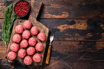 Uncooked Raw meatballs from ground beef and pork meat with rosemary. Dark Wooden background. Top...