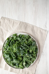 Raw Organic Baby Kale on a gray plate on a white wooden background, top view. Flat lay, overhead, from above. Space for text.