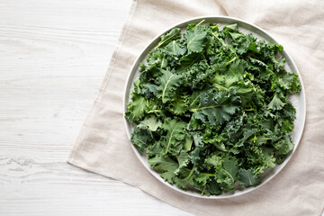 Raw Organic Baby Kale on a gray plate on a white wooden surface, top view. Flat lay, overhead, from above. Copy space.