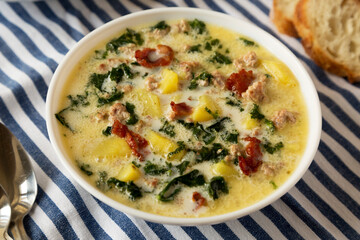 Homemade Zuppa Toscana with Kale and Bread in a white bowl, low angle view.