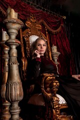 Fototapeta na wymiar Medieval queen in historical attire on golden throne in castle