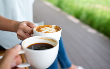 Closeup image of a man and a woman clinking white coffee mugs in the outdoors