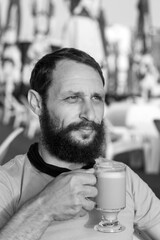 Black and white portrait of handsome bearded man drinking hot, morning espresso coffee with milk looks into the distance In sunset lighting. concept with space for text. Man Holding A Coffee Mug