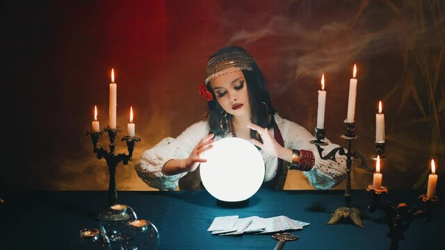 Fantasy witch beautiful gypsy girl, predicts fate, feel energy of crystal ball in dark gothic room. Mystical old art vintage astrology. Fortune teller woman reading future. magic light, tarot cards.