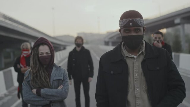 Handheld slowmo shot of group of young male and female protesters in face masks standing on highway outdoors and looking at camera