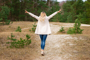 One young beautiful blonde long haired woman with raised hands over green natural forest background outdoor.