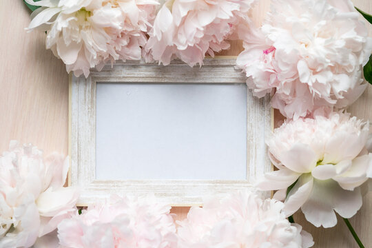 Portrait white picture frame mockup on wooden table. Modern glass vase with peony. White wall background. Scandinavian interior.	